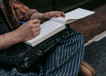 Close-up of a person sitting with a notebook, writing music notes, and holding audio equipment.