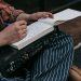 Close-up of a person sitting with a notebook, writing music notes, and holding audio equipment.