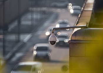 A security camera monitoring activity on a bustling city street with multiple cars in the background.