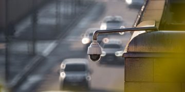 A security camera monitoring activity on a bustling city street with multiple cars in the background.