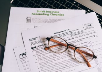 Close-up of tax forms and a small business accounting checklist on a laptop.
