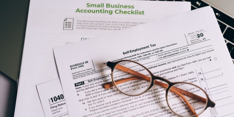 Close-up of tax forms and a small business accounting checklist on a laptop.