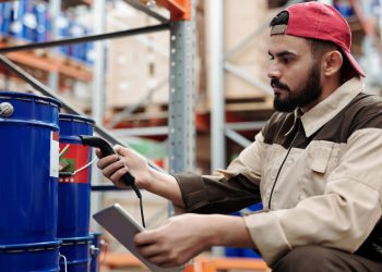 Male warehouse worker scanning barrels with a tablet for inventory management.
