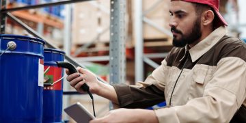 Male warehouse worker scanning barrels with a tablet for inventory management.