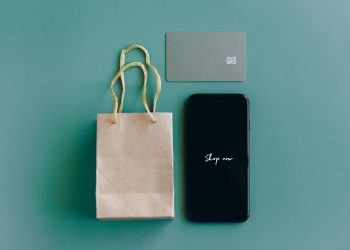 Top view of smartphone with 'Shop now' text, credit card, and paper bag on green background.
