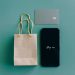 Top view of smartphone with 'Shop now' text, credit card, and paper bag on green background.