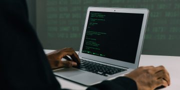 A focused adult working on a laptop demonstrates modern cybersecurity and coding skills indoors.
