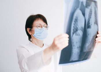 Doctor analyzes lung x-ray wearing a mask in a clinical setting.