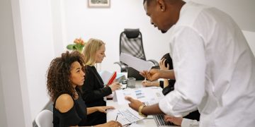An office meeting where a man argues with a woman over documents, causing tension.