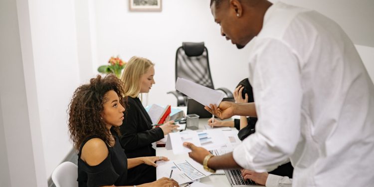 An office meeting where a man argues with a woman over documents, causing tension.