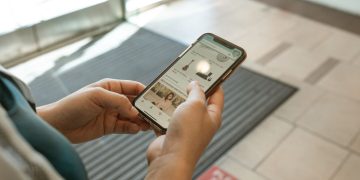 Close-up of hands holding a smartphone displaying an online shopping app in an indoor setting.