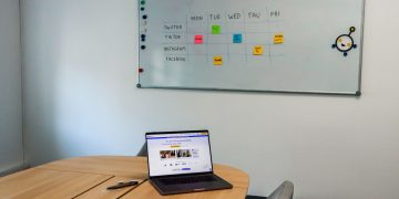 Office setup featuring a conference table, laptop, and organized whiteboard schedule, highlighting a tech-driven workspace.