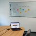 Office setup featuring a conference table, laptop, and organized whiteboard schedule, highlighting a tech-driven workspace.