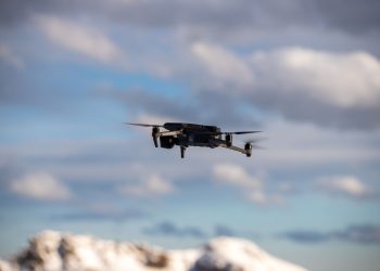 Aerial view of a drone flying over snow-covered mountains with dramatic clouds.
