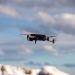 Aerial view of a drone flying over snow-covered mountains with dramatic clouds.