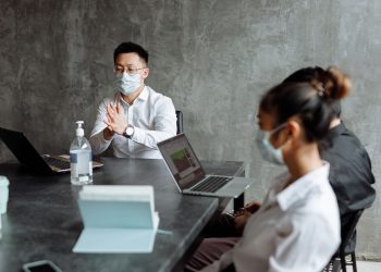 Professionals discussing plans in an office while wearing masks and using laptops.