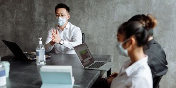 Professionals discussing plans in an office while wearing masks and using laptops.