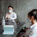 Professionals discussing plans in an office while wearing masks and using laptops.