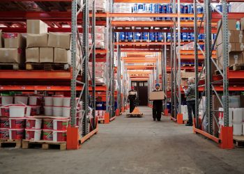 Warehouse interior showing workers handling boxes and organized shelves filled with products.