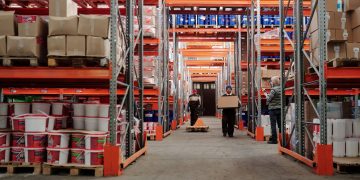 Warehouse interior showing workers handling boxes and organized shelves filled with products.