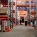 Warehouse interior showing workers handling boxes and organized shelves filled with products.