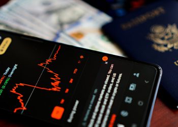 Close-up of a smartphone displaying a stock market app alongside a US passport and currency.