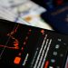 Close-up of a smartphone displaying a stock market app alongside a US passport and currency.