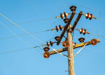 High voltage power line and insulators captured against a clear blue sky.