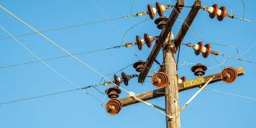 High voltage power line and insulators captured against a clear blue sky.
