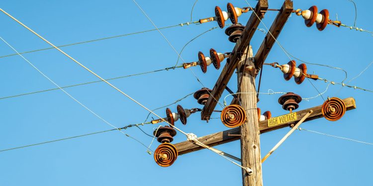 High voltage power line and insulators captured against a clear blue sky.