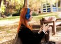 Side profile of a woman with headphones enjoying music on her phone in a sunny autumn park.
