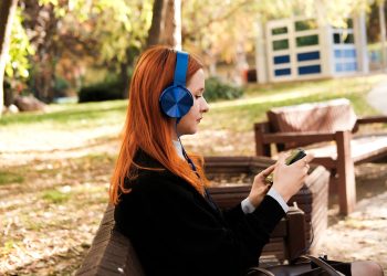 Side profile of a woman with headphones enjoying music on her phone in a sunny autumn park.