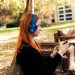 Side profile of a woman with headphones enjoying music on her phone in a sunny autumn park.