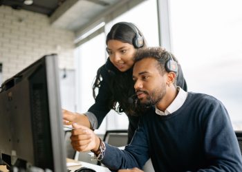 Two call center employees working together with headsets in a modern office setting.