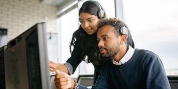 Two call center employees working together with headsets in a modern office setting.