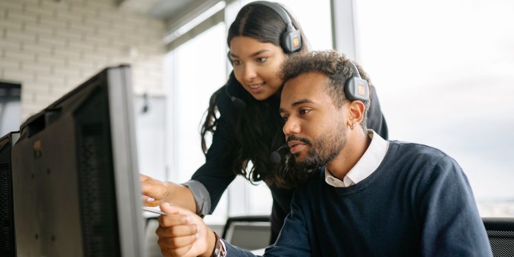 Two call center employees working together with headsets in a modern office setting.