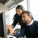 Two call center employees working together with headsets in a modern office setting.