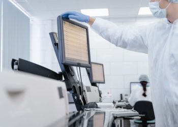 Researcher in PPE reviews data on a digital screen in a modern laboratory setting.
