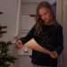 A young girl reads a letter by a decorated Christmas tree indoors.