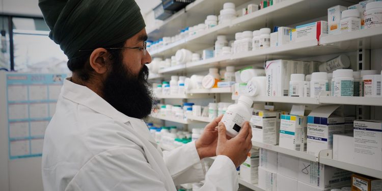 Pharmacist with turban organizing shelves in a pharmacy, focused on healthcare.