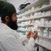 Pharmacist with turban organizing shelves in a pharmacy, focused on healthcare.