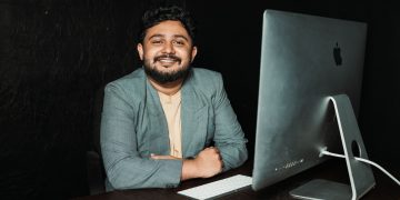 Confident businessman sitting at desk, working on computer in modern office.