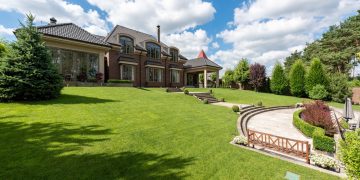 Elegant brick mansion with manicured lawn and garden under a bright blue sky.