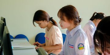 Three young women concentrating on a computer task in a classroom setting.