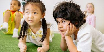 Group of children lying on grass indoors, enjoying a playful learning activity in kindergarten.